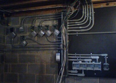 Electrical wires and conduits run along a basement wall, connected to multiple junction boxes.