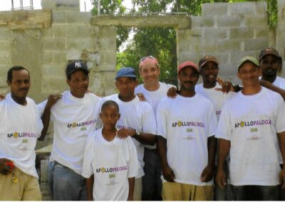 Group of nine people wearing matching "Apollopalooza" T-shirts, standing in front of a partially constructed brick wall. One child is among the group.