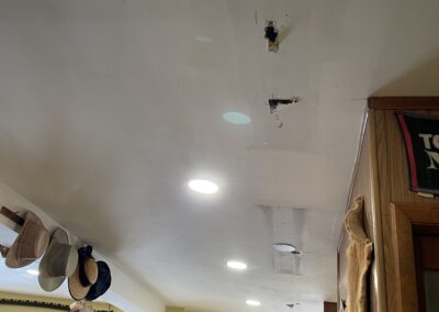 Ceiling with patched areas and recessed lighting in a room with hats on hooks and wall decorations.