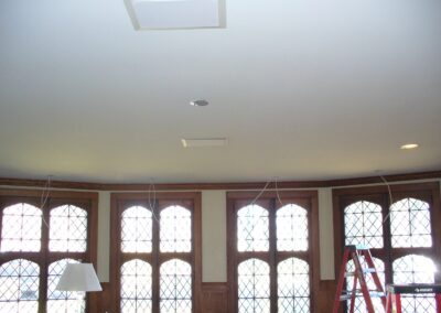 Ceiling with recessed lighting and cables, in a room with tall arched windows and wood paneling. A red ladder is visible.