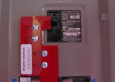 Close-up of an electrical panel with labeled circuit breakers and a red breaker interlock.
