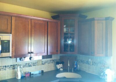 Kitchen corner with wooden cabinets, a microwave, and a tiled backsplash. A dish soap bottle and a Mickey Mouse utensil holder are on the counter.
