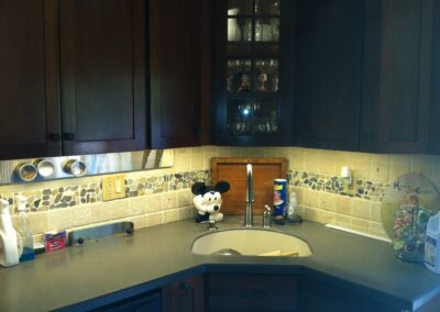 Kitchen corner with dark wood cabinets, beige tile backsplash, and a countertop featuring a Mickey Mouse cookie jar and various kitchen items.